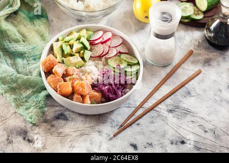 Poke Bowl, tradizionale insalata di pesce grezzo hawaiano con riso, avocado, cetriolo e rafano su sfondo luminoso Foto Stock