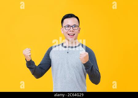Ritratto di felice sorridente vincitore asiatico maschio alzando i pugni isolato su sfondo giallo Foto Stock