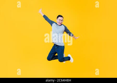 Divertente ritratto di felice uomo asiatico salto in aria con le braccia tese in studio isolato backgorund giallo Foto Stock