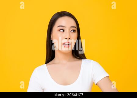 Primo piano ritratto di una giovane donna asiatica curiosa che pensa mentre guarda ansiosamente il lato in uno studio isolato sfondo giallo Foto Stock