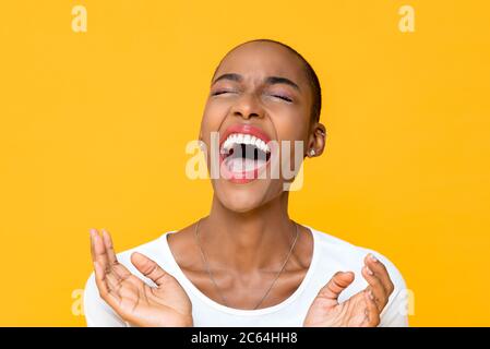 Primo piano ritratto di felice giovane afroamericana donna ridendo forte con entrambe le mani in gesto battente isolato studio sfondo giallo Foto Stock