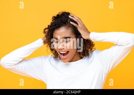 Primo piano ritratto di una donna afro-americana confusa che grida mentre tiene la testa con entrambe le mani in uno sfondo giallo isolato studio Foto Stock