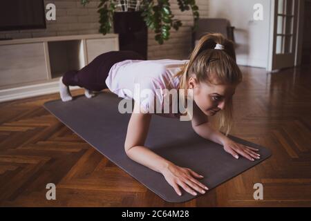 Giovane donna che pratica pilates ed esercizi di yoga a casa. Sta facendo i push-up. Foto Stock