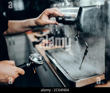 Barista professionista al lavoro con una macchina da caffè - vapore denso in una caffetteria Foto Stock