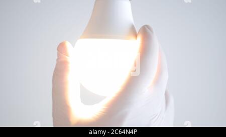 La mano dell'elettricista ruota una lampadina LED nella presa elettrica accendendo la luce Foto Stock