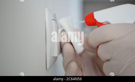 Guanti di protezione uomo-uomo pulizia e disinfezione interruttore luminoso dalla sala ufficio con disinfettante contro i virus Covid-19 Foto Stock