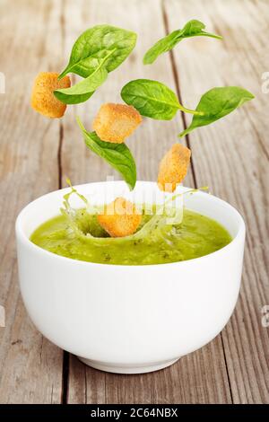 foglie fresche e crostini che cadono in una zuppa verde su un tavolo di legno Foto Stock