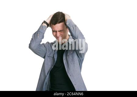 Un giovane uomo in una camicia manaté, t-shirt nera e pantaloni, isolato su bianco. Panics, è sotto stress, tiene la testa con le mani Foto Stock