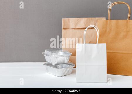 Sacchetti di carta bianca artigianale e contenitori di cibo su sfondo bianco grigio tavola. Servizio di consegna di cibo. Take-away in contenitori di carta stagnola, cartone vuoto Foto Stock
