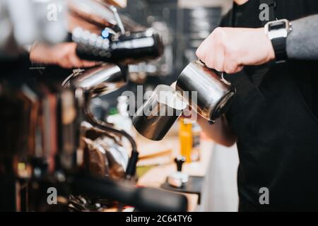 Il barista professionista versa il latte da una caraffa, aggiungendo il latte al caffè Foto Stock