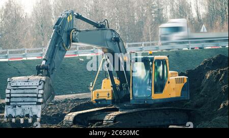 Costruzione della strada. Il lavoro di attrezzature per movimento terra. Escavatore nel processo di livellamento della pendenza della strada e del fossato, impilamento laterale Foto Stock