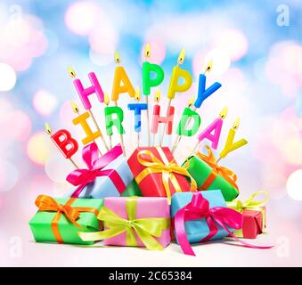 Bruciando candele di compleanno felici con scatole di regalo su sfondo colorato Foto Stock