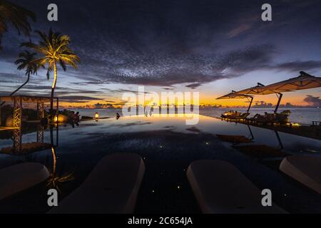 Ammirate un tramonto oltre a una piscina infinity di resort isolani nelle Maldive guardando le palme nell'orizzonte dell'oceano Foto Stock