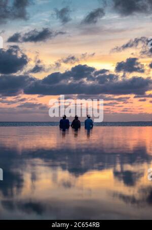 Ammirate un tramonto oltre a una piscina infinity di resort isolani nelle Maldive guardando le palme nell'orizzonte dell'oceano Foto Stock