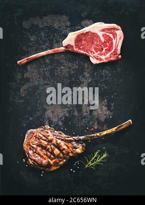 Black angus Tomahawk bistecche di manzo crude e grigliate con condimento su sfondo rustico scuro Foto Stock