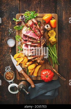 Carne alla griglia, ​​tomahawk bistecca di manzo affettata con spezie, patatine fritte e verdure su sfondo rustico Foto Stock