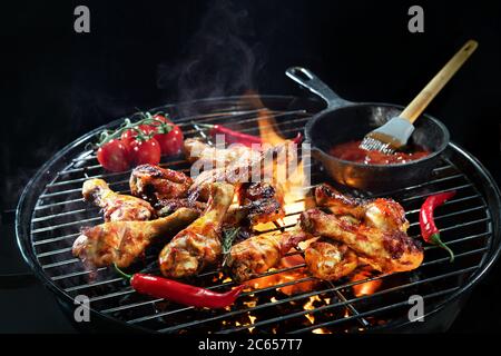 Cosce di pollo o bastoncini di pollo grigliati sulla griglia con barbecue caldo e acceso con fumo su sfondo scuro Foto Stock