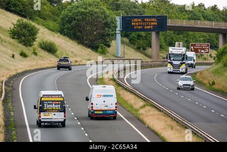 East Lothian, Scozia, Regno Unito, 7 luglio 2020. Covid-19 nuovo messaggio sul gantry A1: La terza versione del messaggio pandemico viene visualizzata sul gantry sospeso vicino a Haddington che recita "restrizioni locali di viaggio rimanere sicuri", poiché la Scozia si allena nella fase 3 prevista la prossima settimana. Il traffico sulla carreggiata a doppia carreggiata è molto più pesante di quanto si sia visto negli ultimi mesi Foto Stock