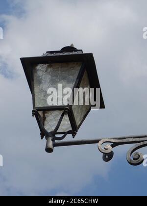 Vista di una bella vecchia lanterna di ferro appesa di fronte ad un edificio contro un cielo nuvoloso in un villaggio in Italia Foto Stock