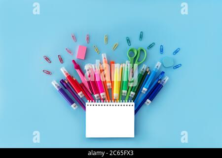 Ritorno a scuola con blocco note aperto e varietà di forniture scolastiche in colori arcobaleno su sfondo blu pastello. Disposizione piatta. Primo piano. Spazio di copia. Foto Stock