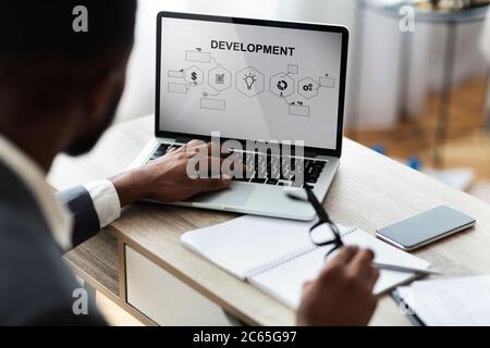 Uomo d'affari che crea il programma di sviluppo di affari su laptop seduto in ufficio Foto Stock