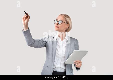 Donna d'affari intelligente con tablet che scrive qualcosa sullo schermo immaginario su sfondo chiaro, mockup per il design Foto Stock