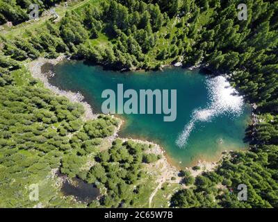 Vista aerea di un lago di montagna blu e limpido circondato da verdi foreste di conifere in una giornata soleggiata scattata da un drone Foto Stock