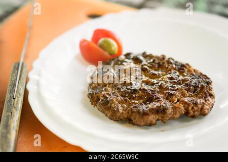 Polpettine di hamburger di manzo cotto su un piatto servito con pomodoro fresco e olive in primo piano con un coltello a fianco Foto Stock