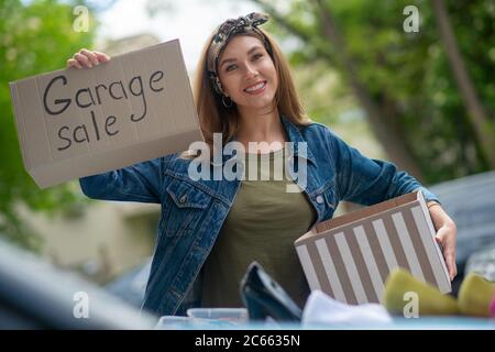 Donna giovane graziosa che tiene un segno di vendita del garage Foto Stock