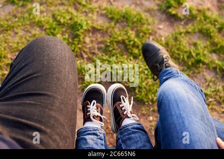 Le gambe di mamma, papà e bambino sullo sfondo di erba verde. La famiglia trascorre il tempo insieme. Primavera Foto Stock