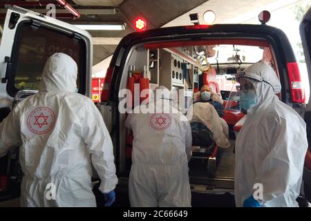 Rivestimento testa a piedi in dispositivi di protezione paramedici di MDA Magen David Adom emergenza servizio medico evacuare un paziente anziano sospettato di avere COVID-19 in un ospedale a Gerusalemme. Foto Stock