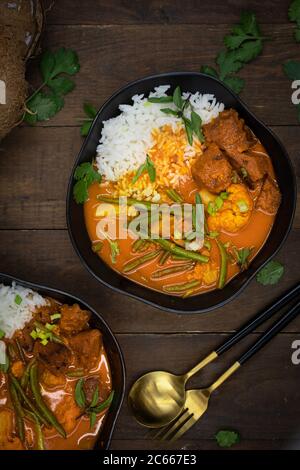 Curry rosso thai vegano con seitan, fagioli e cavolfiore su riso, servito in ciotole nere Foto Stock