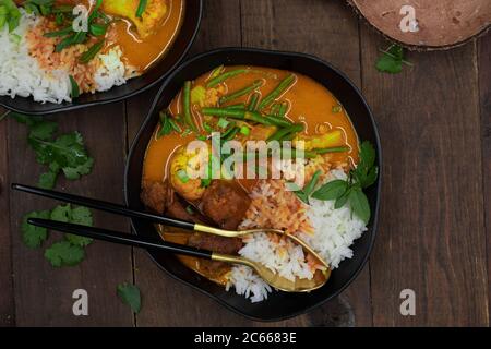 Curry rosso thai vegano con seitan, fagioli e cavolfiore su riso, servito in ciotole nere Foto Stock