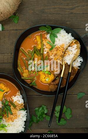 Curry rosso thai vegano con seitan, fagioli e cavolfiore su riso, servito in ciotole nere, spazio copia Foto Stock