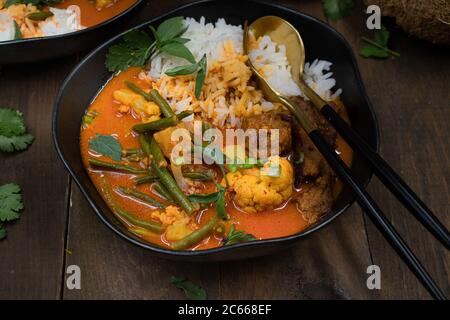 Curry rosso thai vegano con seitan, fagioli e cavolfiore su riso, servito in ciotole nere Foto Stock