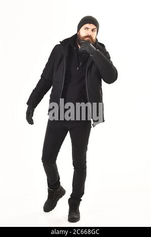 Macho con barba e baffi indossa giacca invernale, guanti, cappello. Uomo con volto pensieroso, isolato su sfondo bianco. Concetto di abbigliamento invernale. Ragazzo in nero e vestito in movimento, a piedi. Foto Stock