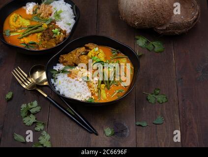 Curry rosso thai vegano con seitan, fagioli e cavolfiore su riso, servito in ciotole nere, spazio copia Foto Stock
