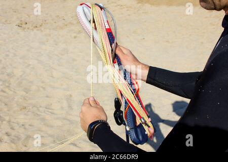 primo piano un uomo lancette rotolando un kite bar e linee sulla spiaggia dopo kitesurf. Attrezzatura per kitesurf per corsi di kite. Sport acquatici estremi. Lo selvaggio Foto Stock