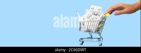 Vista laterale di una mano donna che spinge e rotola un mini carrello pieno di pillole. Il concetto di online shopping medicina su sfondo blu. P. Online Foto Stock