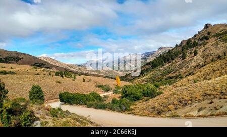 Strada che conduce attraverso il paesaggio roccioso, circondato da alberi e cespugli in Argentina Foto Stock