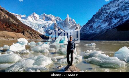 Persona in piedi sulla Laguna Cerro Torre con galleggianti di ghiaccio in acqua, circondato da montagne innevate, Argentina Foto Stock