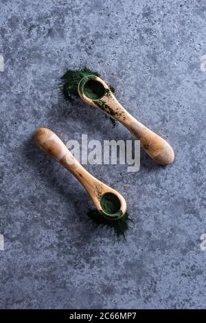 Polvere naturale di clorella o spirulina in due cucchiai di legno. Una certa polvere cade dai cucchiai. Concetto sano di alimentazione e dieta di superfood. Blu g Foto Stock