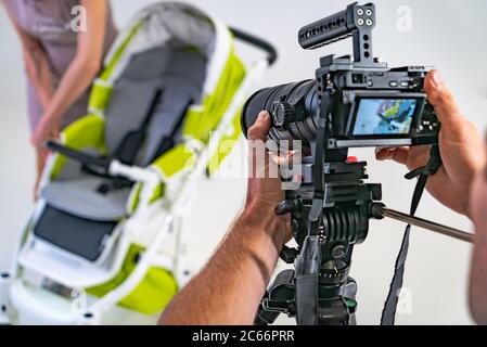 un fotografo spara la madre con il carrello del bambino. Una donna in abito rosa prepara un passeggino per camminare. Foto Stock