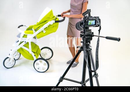 una giovane madre in un vestito rosa tiene per mano la maniglia di un passeggino. Uno schermo della fotocamera è messo a fuoco sulla donna su uno sfondo bianco. Foto Stock