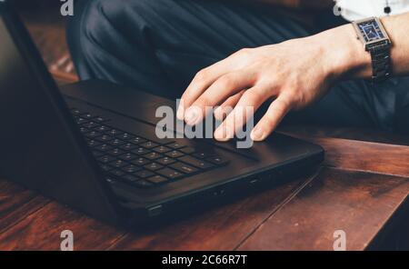 una mano dell'uomo con un orologio da polso si trova sul touchpad del laptop. Uomo d'affari lavora a casa nella sua stanza. Foto Stock