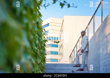 Uomo d'affari afro-americano al tramonto in un parco. Sta crogiolandosi al sole della sera. Foto Stock