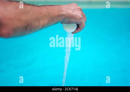 Persona che pulisce e clorurando la piscina in un caldo pomeriggio estivo, sta facendo funzionare il pulitore e aggiungendo polvere di cloro Foto Stock