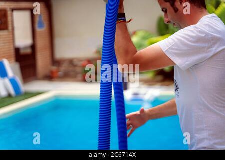 Persona che pulisce e clorurando la piscina in un caldo pomeriggio estivo, sta facendo funzionare il pulitore e aggiungendo polvere di cloro Foto Stock