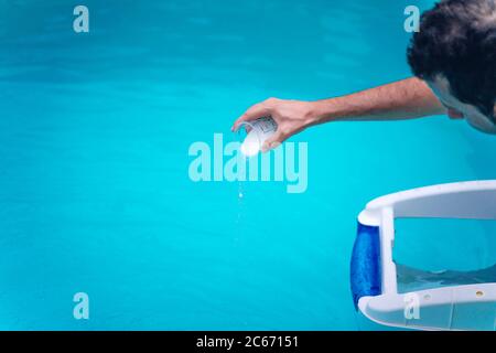 Persona che pulisce e clorurando la piscina in un caldo pomeriggio estivo, sta facendo funzionare il pulitore e aggiungendo polvere di cloro Foto Stock