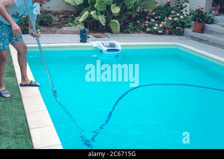Persona che pulisce e clorurando la piscina in un caldo pomeriggio estivo, sta facendo funzionare il pulitore e aggiungendo polvere di cloro Foto Stock